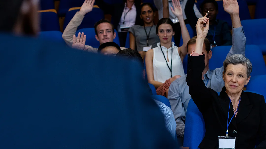 Une femme lève la main devant un groupe de personnes lors d'un congrès.