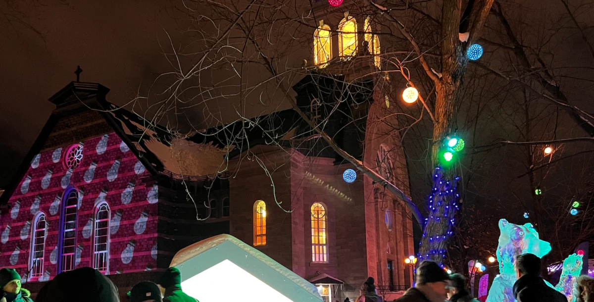 Capture-decran-le-2023-02-01-a-08.28.08-e1744220063213 Une église ornée de projections lumineuses et d'ice sculptures, entourée de gens et de lumières colorées.